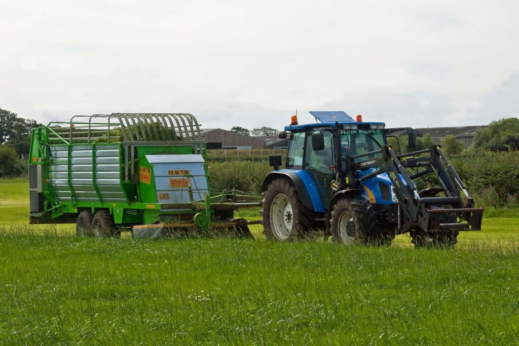 Blue tractor pulling a green forage wagon